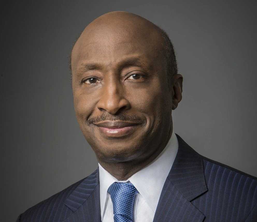 A black man in a suit and tie smiling in front of a plain background