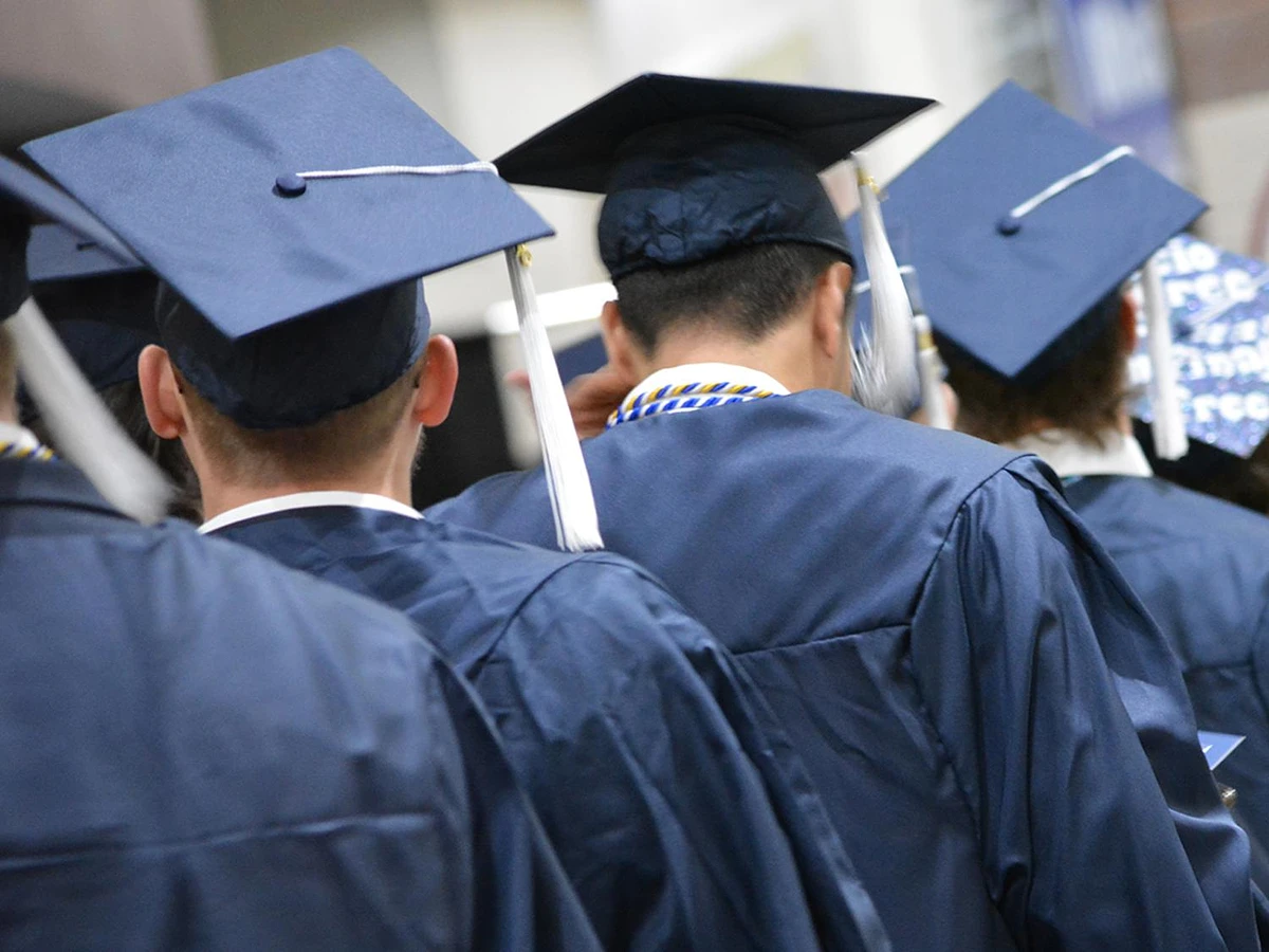 The back of of 3 students walking away in a line wearing blue academic regalia.