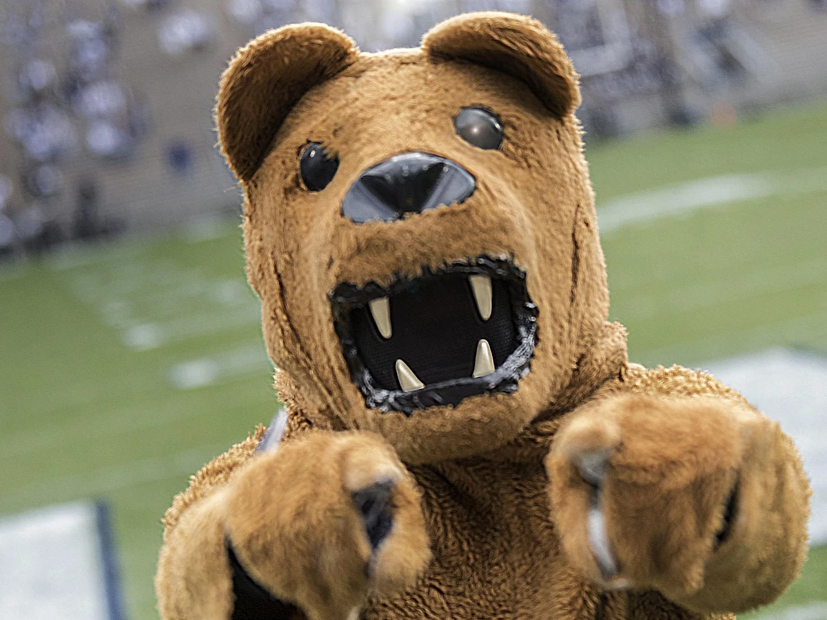 Nittany Lion mascot face close up pointing both fingers at the camera with a football field in the background.