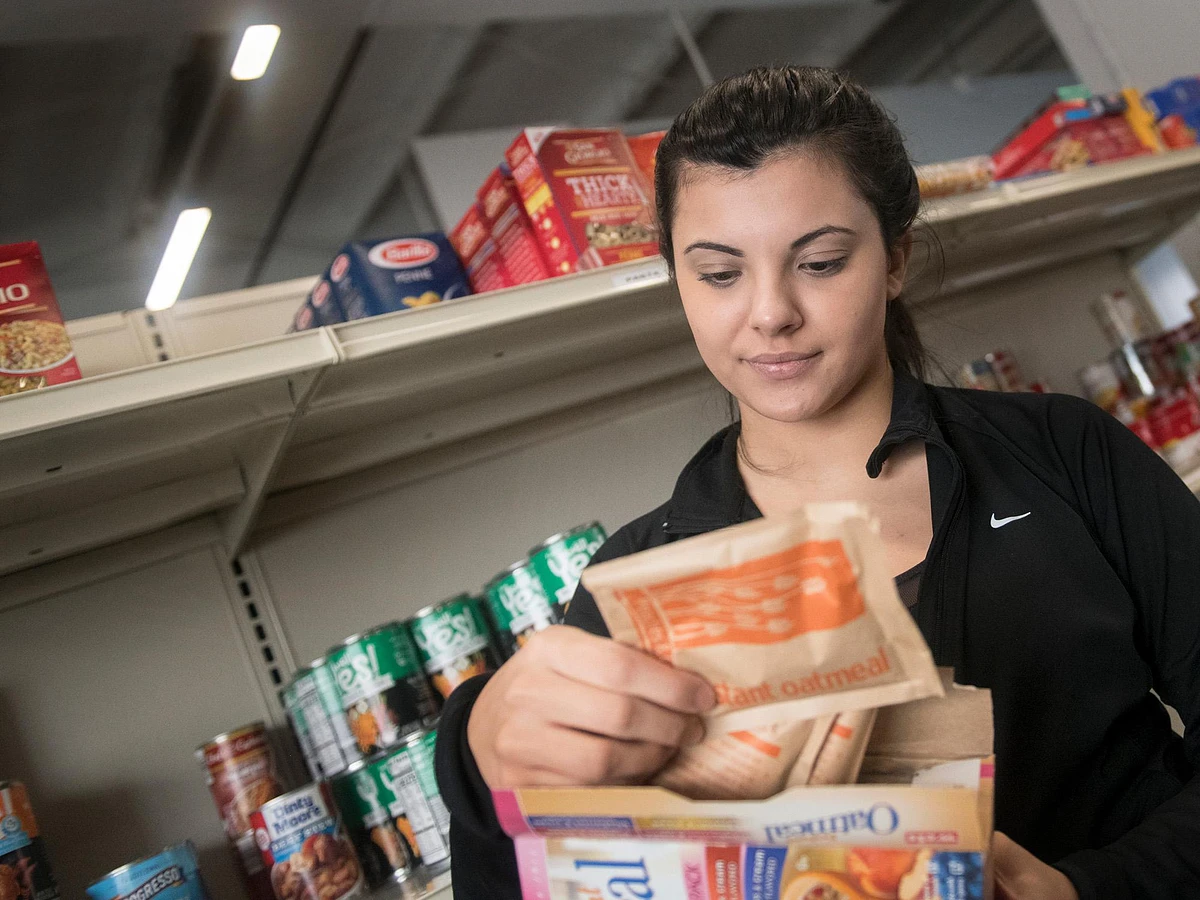 Student reading back of food packaging in front of food shelves.