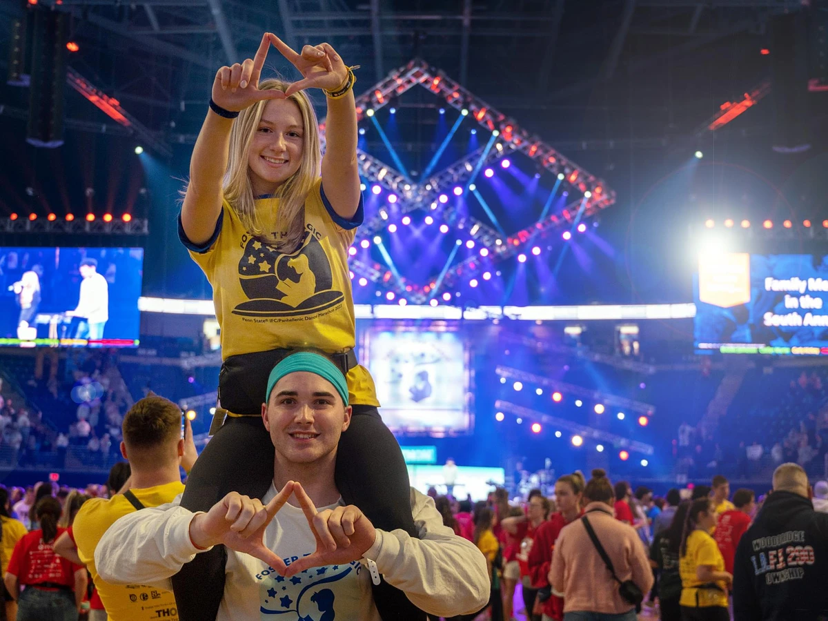 2 students dancing at Thon making a diamond symbol with their hands.