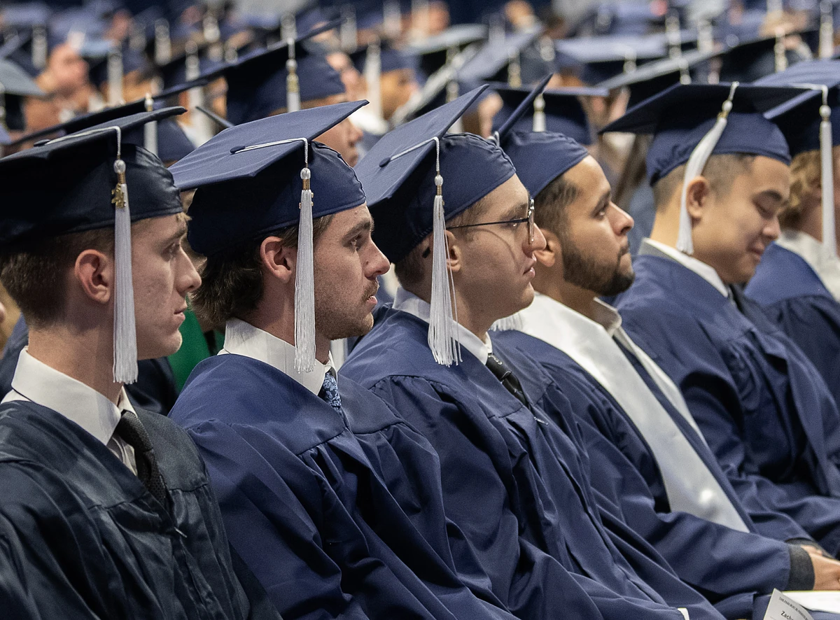 A group of graduates in caps and gowns sit attentively at a commencement ceremony.