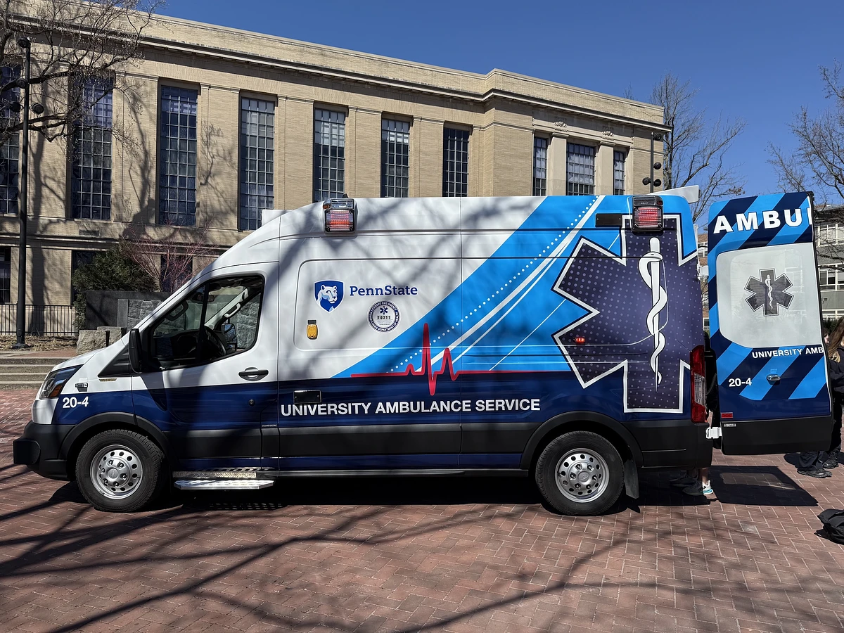 A Penn State University ambulance is parked in front of a large building on a sunny day.
