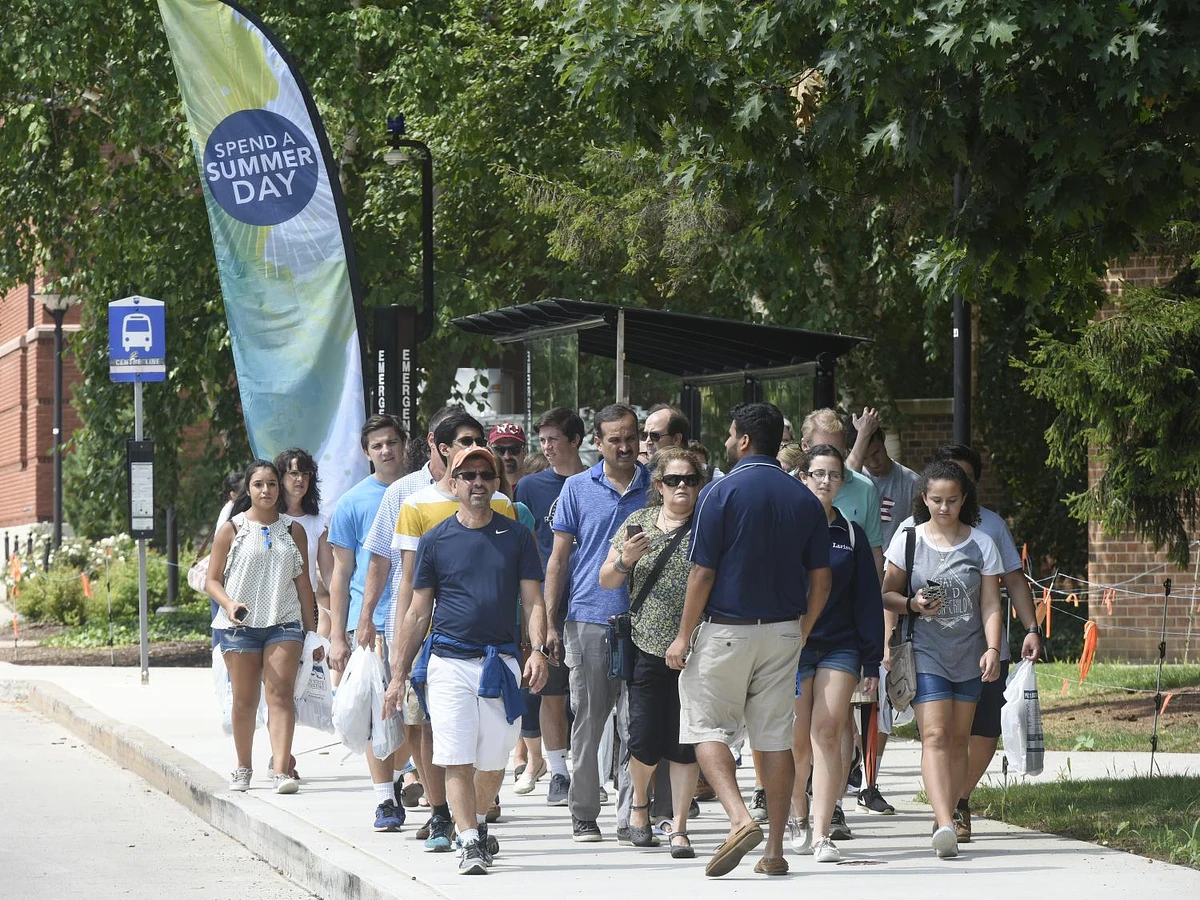 A group of people is walking together on a sidewalk near a "Spend a Summer Day" banner.