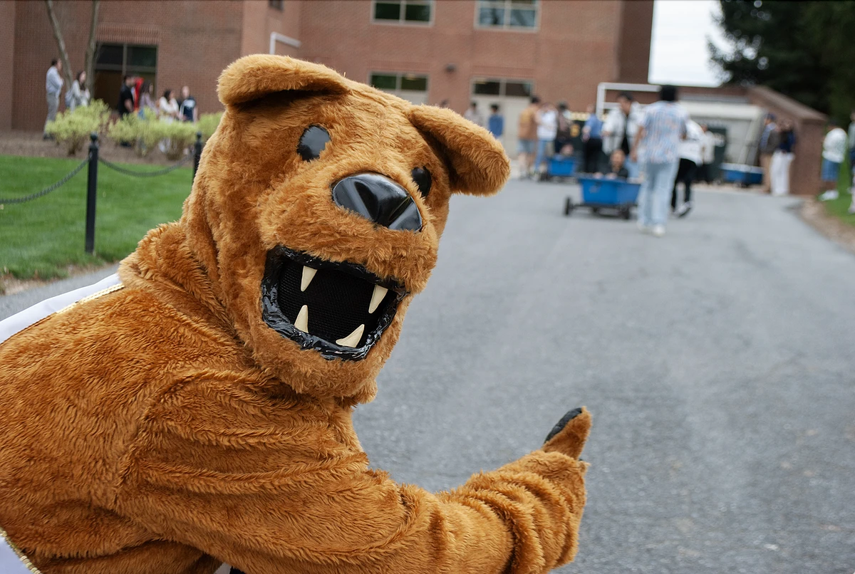 A person in a lion costume gives a thumbs-up while people gather in the background.